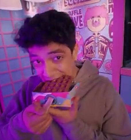 photo credit: Ashol Waffle Up Chinum by Waffle Up. Man eating a chocolate dipped waffle on a stick in a special cardboard container that has a hole for the stick.